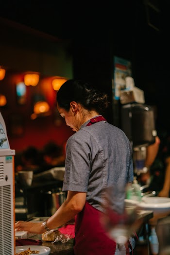 Person Wearing Red Apron Stands in Front of Table With Plate
