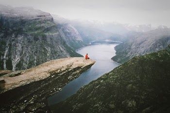 person wearing red shirt sitting on the boulder near the mountain