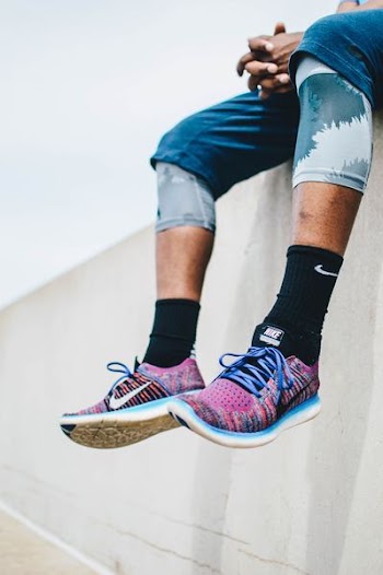 person wearing running shoes sitting on concrete pavement