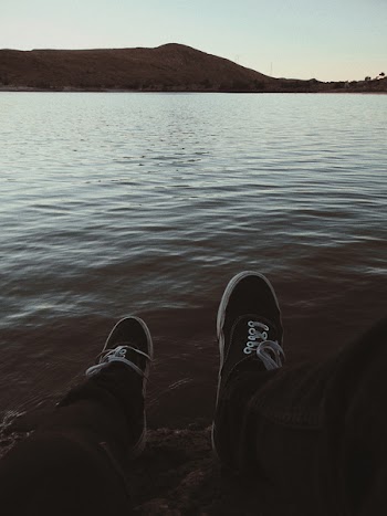 Person Wearing Sneakers Sitting in Front of Ocean