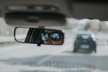 Person Wearing Sunglasses Sitting Inside Car Viewed on Vehicle Rear View Mirror