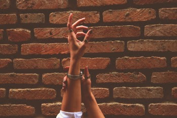 Person Wearing Watch and Rings Raising Left Hand Near Brick Wall