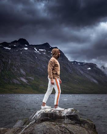 Person Wearing White and Orange Sweat Pants and Brown Sweatshirt Standing on Rock Near Body of Water