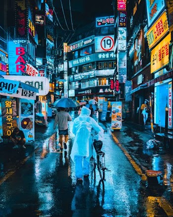 person wearing white raincoat on street while holding bicycle between high-rise building