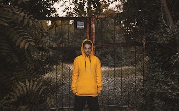 Person Wearing Yellow Hoodie Standing Beside Black Metal Gate