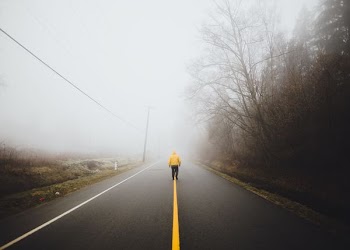 person wearing yellow jacket walking on empty road