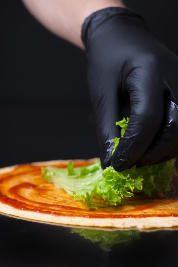 Person With Gloves Putting Lettuce on Pizza