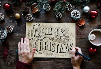 person writing Merry Christmas on paper in between Christmas decors
