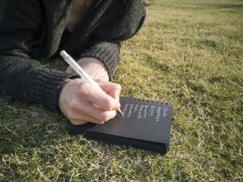Person Writing on Book Lying Down on the Ground