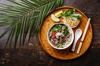 Pho Bo vietnamese Soup with beef on bamboo tray and palm branch on wooden background