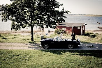 Photo of a Couple  Beside Parked Black Classic Roadster Near  Beach