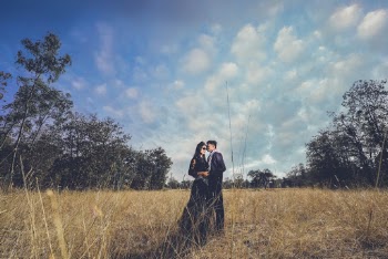 Photo of a couple holding each other standing on brown grass field