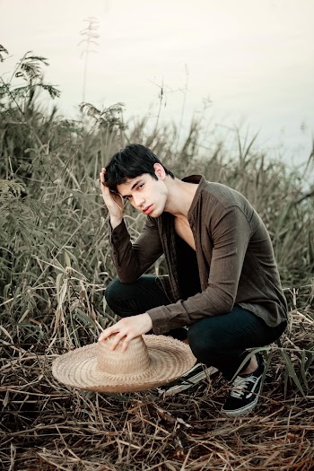 Photo of a man crouching while holding a sun hat