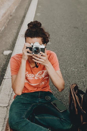 Photo of a Man  Sitting on Road Using His Camera With His Smartphone on His Lap