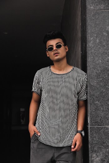 Photo of a Man Wearing a Striped Crew Neck T-Shirt  Leaning on a Wall