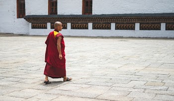 Photo of a Monk Walking on a Concrete Pavement
