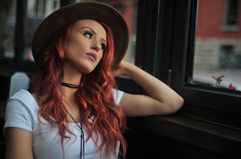 Photo of a red-haired woman looking outside a glass window