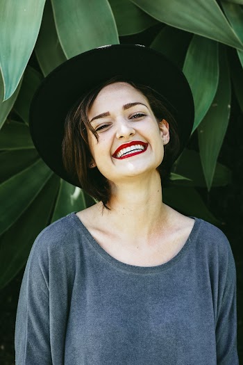 Photo of a Smiling Woman Wearing Gray Top and Black Hat