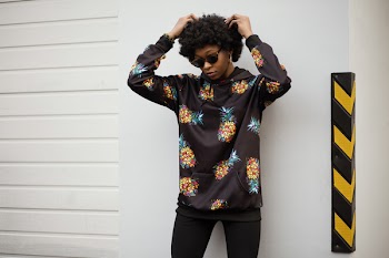 Photo of a Woman in Pineapple Print Pullover Leaning on White Wall