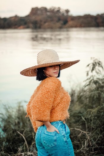 Photo of a Woman in Sun Hat, Orange Knitted Top, and Blue Denim Bottoms