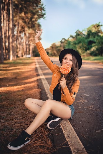 Photo of a woman sitting down on the road licking a swirl lollipop