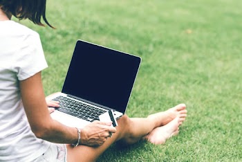 Photo of a Woman Sitting on Lawn Grass  Holding Card with Mac book air on Laps 