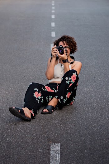 Photo of a Woman Sitting on Road Holding Camera