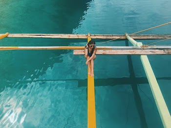Photo of a Woman Sitting on Wooden Boat's Outrigger
