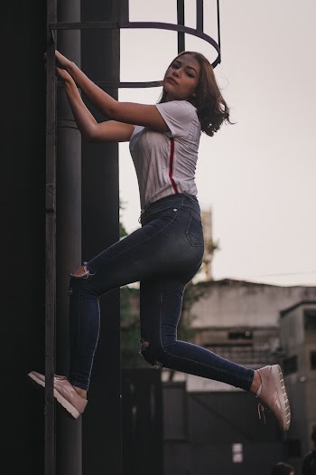 Photo of a Woman Stepping and Holding on a Metal beside a building