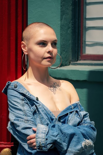 Photo of a woman wearing a blue denim jacket standing near a window  