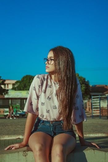 Photo of a Woman Wearing a pink top and shorts sitting down looking away