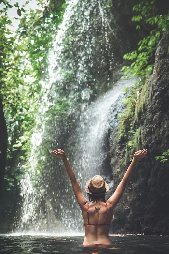 Photo of a woman wearing a red bikini standing in the water near a waterfall