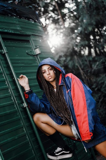 Photo of a woman wearing an orange and blue jacket leaning on a green steel door