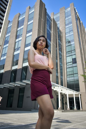 Photo of a woman wearing pink standing in front of gray buildings