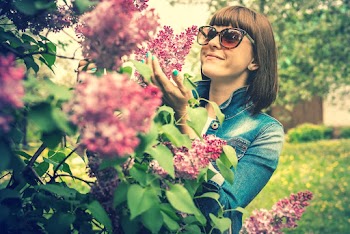 Photo of a woman wearing sunglasses holding lilac flowers