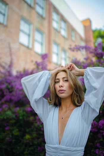 Photo of a Young Woman in a White Shirt with Purple Flowers in the Background