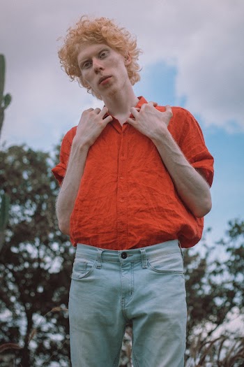 Photo of Albino Man Wearing Orange Shirt and Blue Denim Jeans Standing