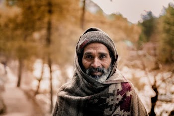 Photo of an elderly man smiling wearing  a knit cap and scarf 