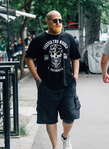 Photo of Bald Tattooed Man Walking on Side Walk