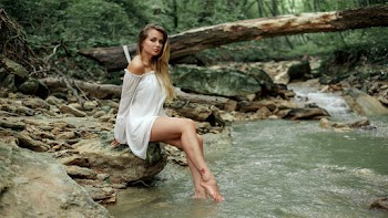 Photo of Beautiful Woman in White Dress Sitting On Rock Beside Stream Posing