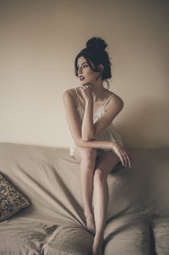 Photo of Beautiful Woman in White Night Dress Sitting on Top of Sofa Backrest Looking Away