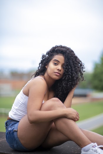 Photo of Beautiful Woman in White Top and Blue Denim Shorts Posing While Sitting