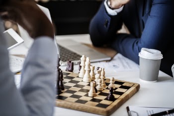 Photo of Brown Wooden Chess Set on Table Beside White and Gray Disposable Cup