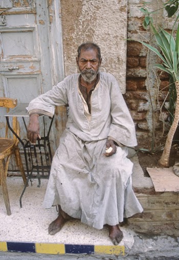Photo of Elderly Man in Beige Thobe Sitting Alone Outside a Building