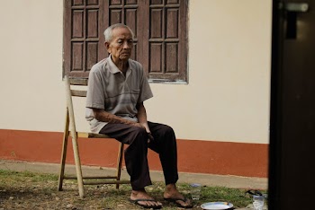 Photo of Elderly Man Sitting on Wooden Chair Outside House