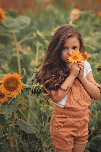 Photo of Girl in Orange Dungaree Holding Sunflower