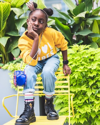 Photo of Girl in Yellow Sweatshirt, Blue Jeans, and Black Leather Sitting on Backrest of Yellow Chair Posing
