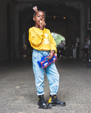 Photo of Girl in Yellow Sweatshirt, Blue Jeans, and Black Posing Alone While Applying Lip Balm
