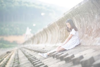 Photo of Girl Sitting Alone on the Ground Leaning Against Concrete Barrier