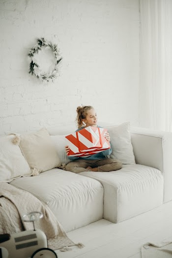 Photo of Girl Sitting on White Sofa with Her Legs Crossed Holding Present